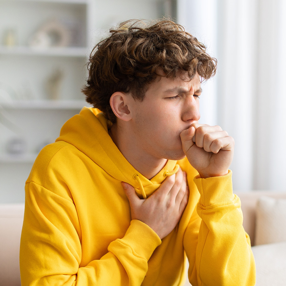 Ein Teenager der hustet und seine Hand vor dem Mund hat.