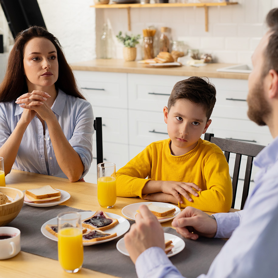 Familie sitzt beim Frühstück an einem Tisch und diskutiert.