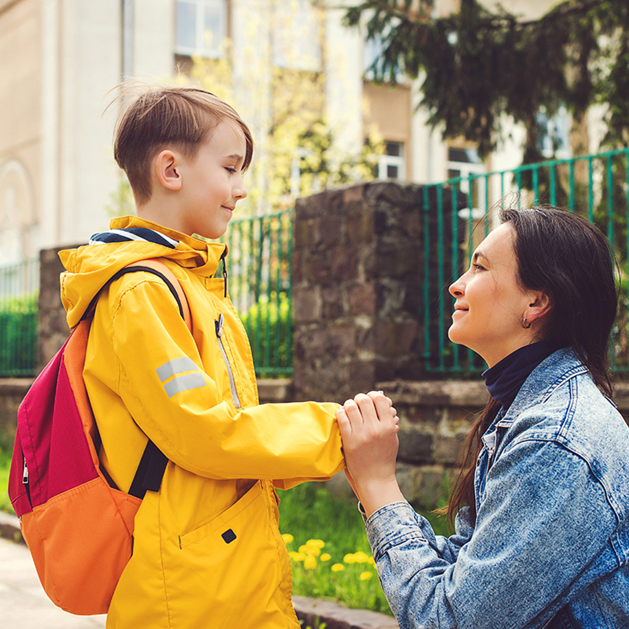 Eine Mutter hält die Hand ihres Sohnes. Er hat einen Rucksack auf.