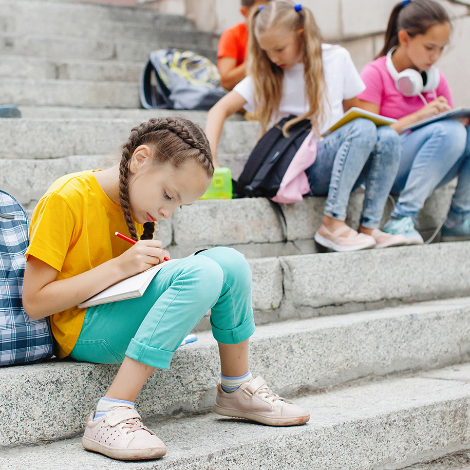 Ein Mädchen sitzt alleine auf einer Treppe und schreibt etwas in ein Buch.