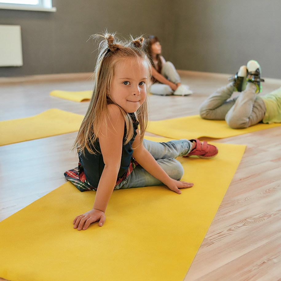Ein kleines Mädchen liegt auf einer gelben Sportmatte.