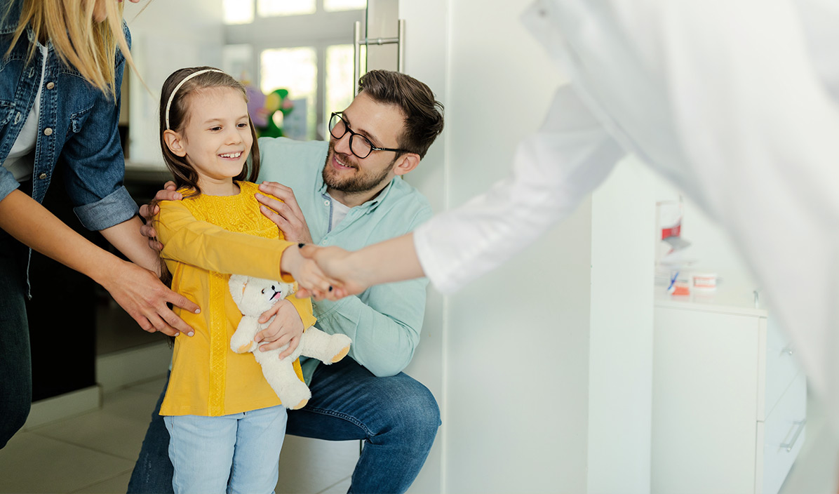 Ein Arzt steht an der Tür einer Familie und schüttelt die Hand eines Kindes.