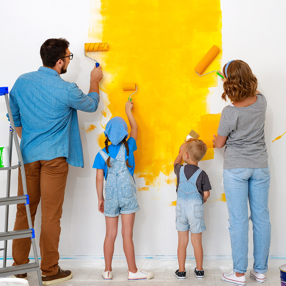 Eltern streichen mit ihren beiden Kindern eine weiße Wand gelb.