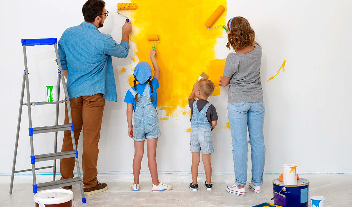 Eltern streichen mit ihren beiden Kindern eine weiße Wand gelb.