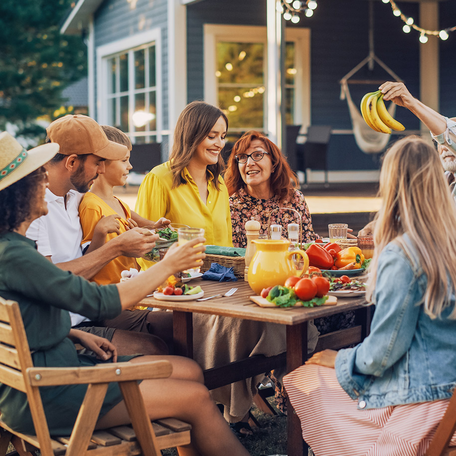 Familie und Freunde sitzen an einem Gartentisch und essen.